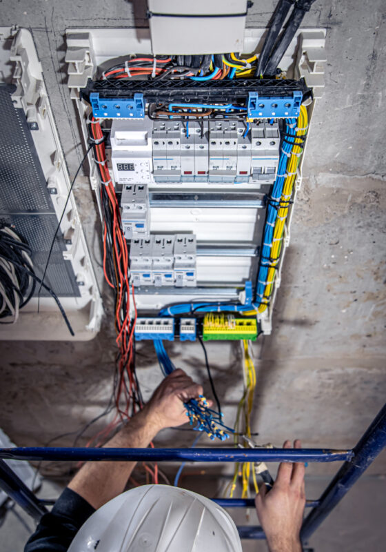 A male electrician works in a switchboard with an electrical connecting cable, connects the equipment with tools, top view.