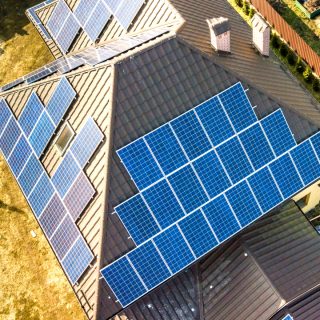 Aerial top view of new modern residential house cottage with blu Aerial top view of new modern residential house cottage with blue shiny solar photo voltaic panels system on roof. Renewable ecological green energy production concept.